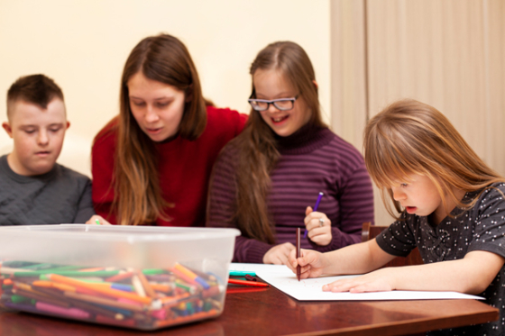 Children with down syndrome sitting with a teacher around a table, doing a drawing workshop. Credit: Freepik