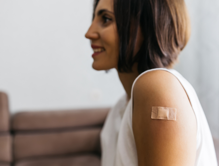 Woman smiling, bandage on arm having received vaccine. Credit: AdobeStock