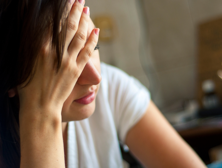 Tired looking woman with hand against forehead