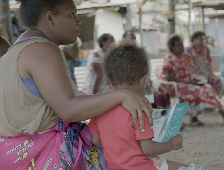 Vanuatu woman with child outside reading cervical cancer information brochure