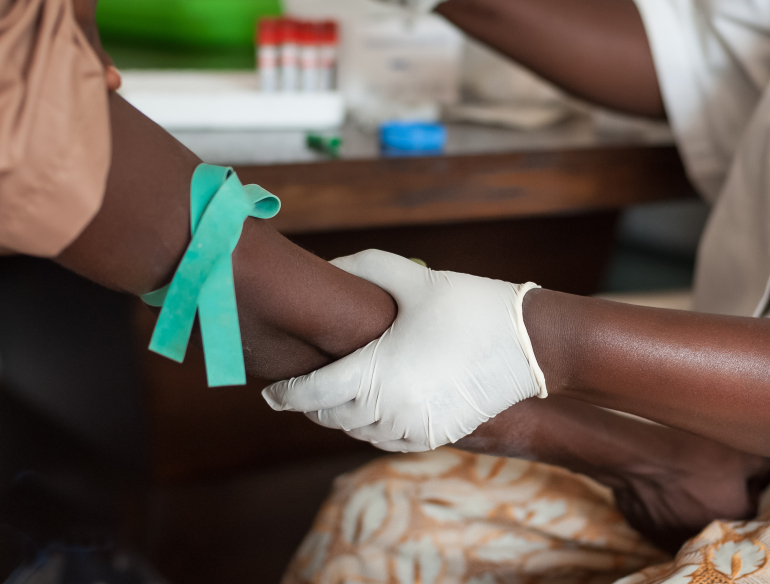 Two dark skinned people at a medical examination, where one is taking a blood sample from the other. Credit: Shutterstock.