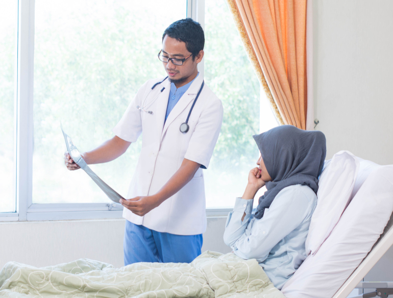 Man doctor showing xray to woman in hijab lying in hospital bed. Credit: AdobeStock