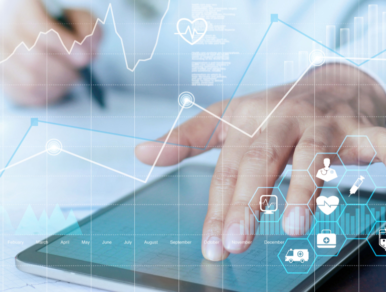 Graphs and medical symbols overlayed over a medical staff member writing, one hand touching a tablet. Credit: AdobeStock.