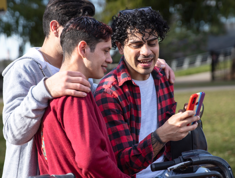 Group of young gay men huddled together, looking at mobile phone. Credit: AdobeStock