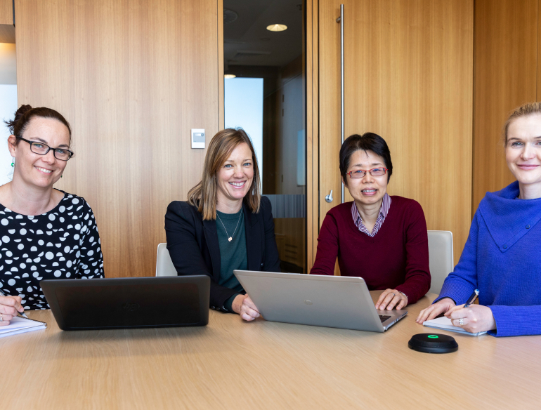 Group of women staff, clinical trial coordinators sitting around at a table with laptop. Credit: Kirby Institute/Bec Lewis