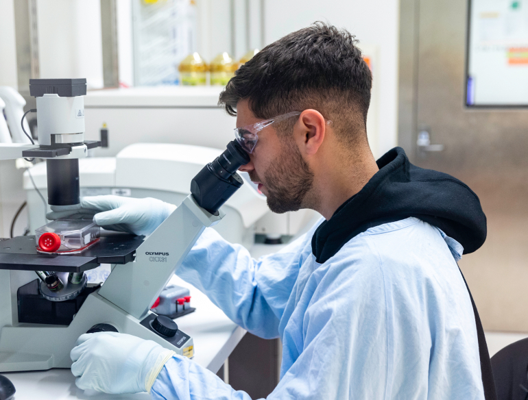 Lab technician looking at specimen through a microscope. Credit: Kirby Institute/Bec Lewis.