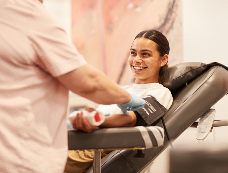 A smiling woman blood donor sitting in a chair with a collector. Credit: Lifeblood.