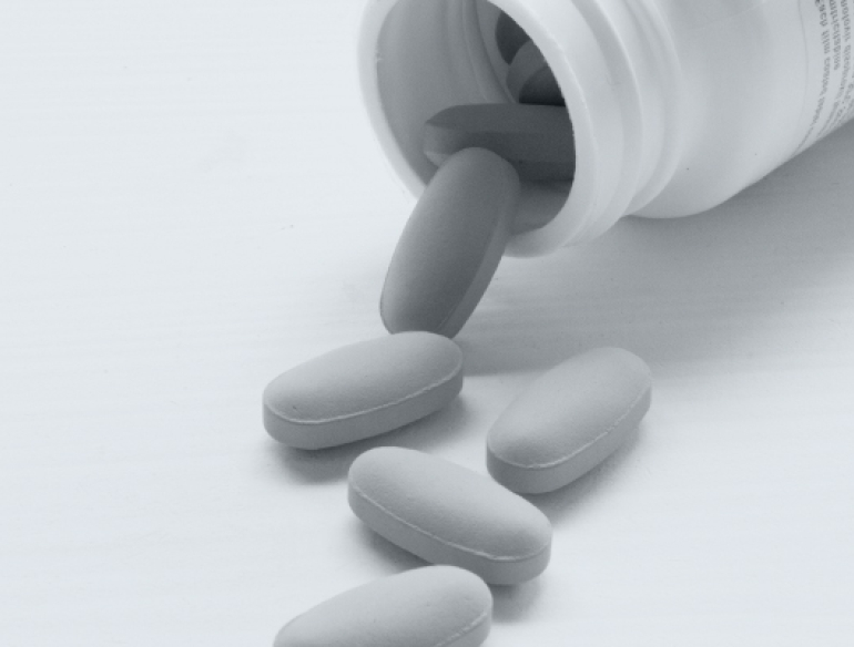 Black and white image of a medication bottle laying open on a surface, with 5 pills spilling out