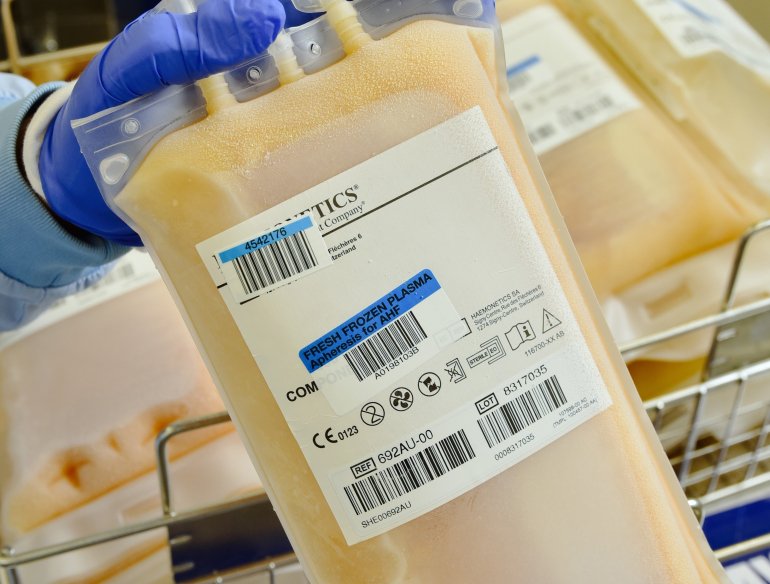 Medical bag of frozen plasma held by purple gloved hands. Credit: LifeBlood