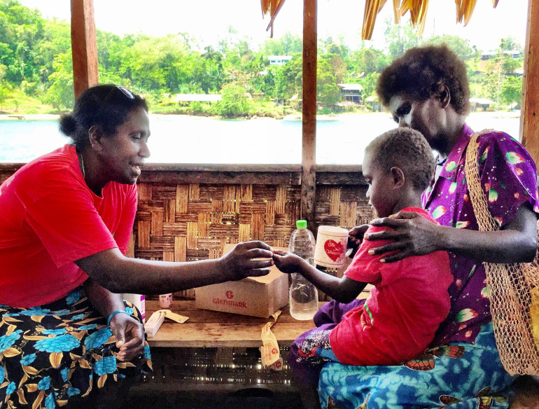 Woman giving medication to a child and mother, Solomon Islands.