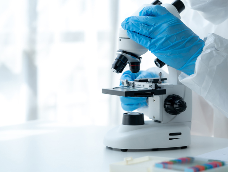 A person wearing protective gear and blue gloves holds a microscope