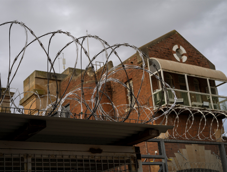 Barbed wire in foreground and brick prison building in background