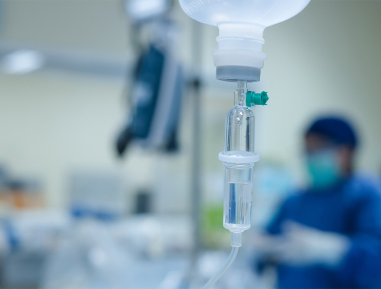 Shot of IV in focus with a medical profession in blue scrubs in the blurred background