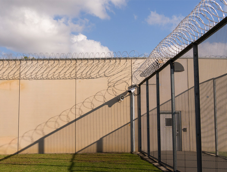 outside setting of a prison, with fencing topped by barbed wire