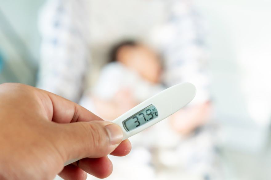 Thermometer being held in foreground patient in bed in background
