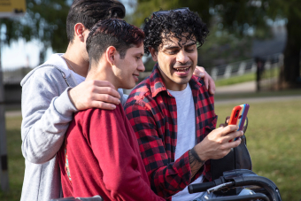 Group of young gay men huddled together, looking at mobile phone. Credit: AdobeStock