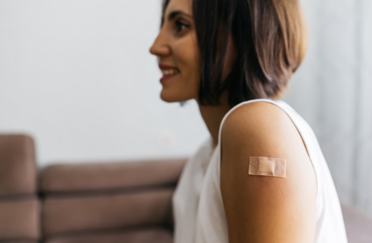 Woman smiling, bandage on arm having received vaccine. Credit: AdobeStock