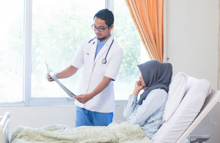 Man doctor showing xray to woman in hijab lying in hospital bed. Credit: AdobeStock