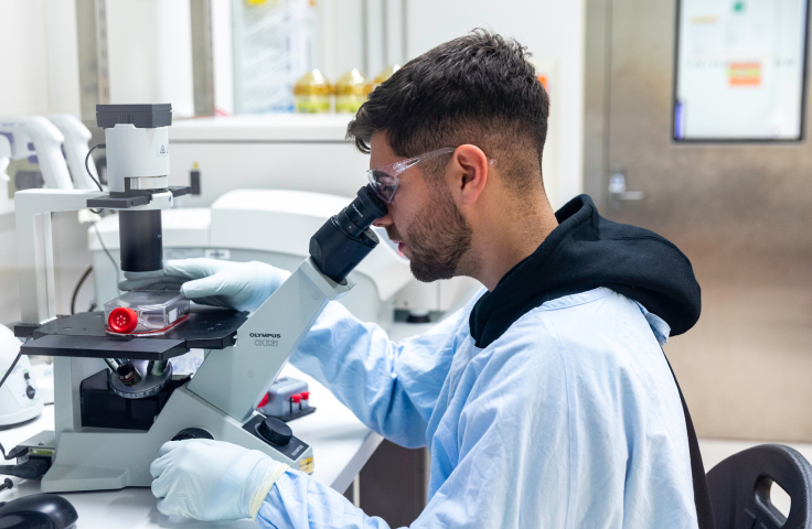 Lab technician looking at specimen through a microscope. Credit: Kirby Institute/Bec Lewis.