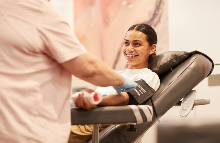 A smiling woman blood donor sitting in a chair with a collector. Credit: Lifeblood.