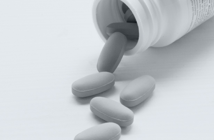Black and white image of a medication bottle laying open on a surface, with 5 pills spilling out