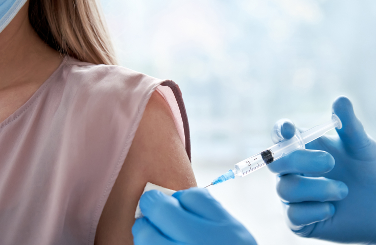 Vaccination of a masked woman. Medical professional injecting vaccine syringe into arm. Credit: iStock