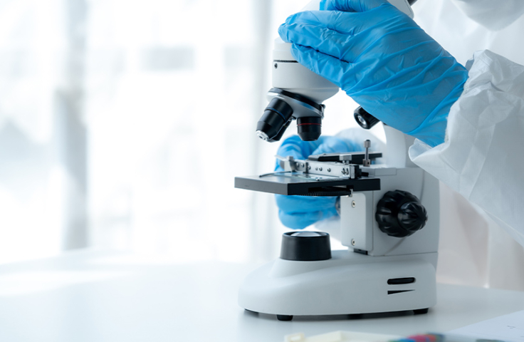 A person wearing protective gear and blue gloves holds a microscope
