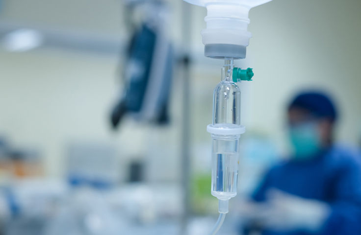 Shot of IV in focus with a medical profession in blue scrubs in the blurred background