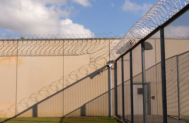 outside setting of a prison, with fencing topped by barbed wire